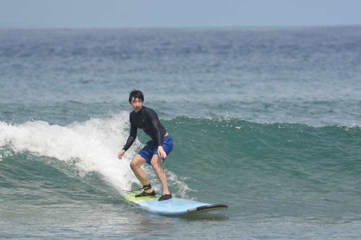 Person surfing on a wave with a blue surfboard, wearing a wetsuit and blue shorts.