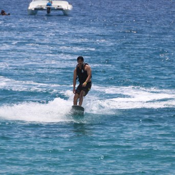Person wakeboarding on the ocean, with a boat and swimmers in the background.