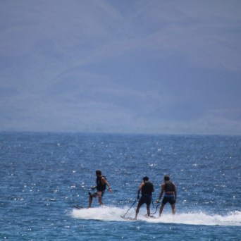 Three people jet skiing together on a calm ocean with hills in the background.