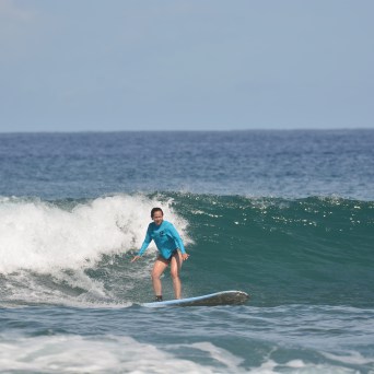 Person surfing on a blue ocean wave under a clear sky.