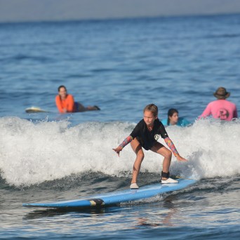 Child surfing a wave on a blue surfboard with people in the background.