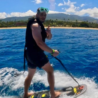 Person on a jetboard in the ocean near a sandy beach with mountains in the background.